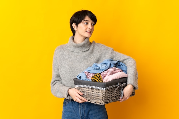 Jovem mulher segurando uma cesta de roupas olhando de lado