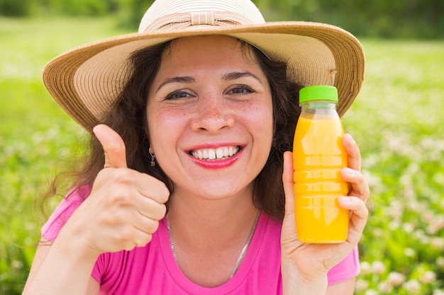 Jovem mulher segurando uma garrafa com suco e mostrando os polegares para cima gesto.