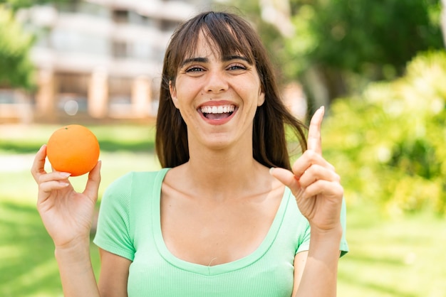 Jovem mulher segurando uma laranja ao ar livre apontando uma ótima ideia