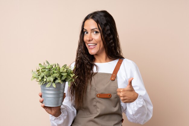 Jovem mulher segurando uma planta com polegares para cima porque algo bom aconteceu