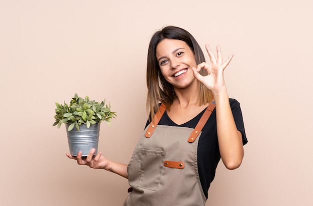 Jovem mulher segurando uma planta mostrando sinal de ok com os dedos