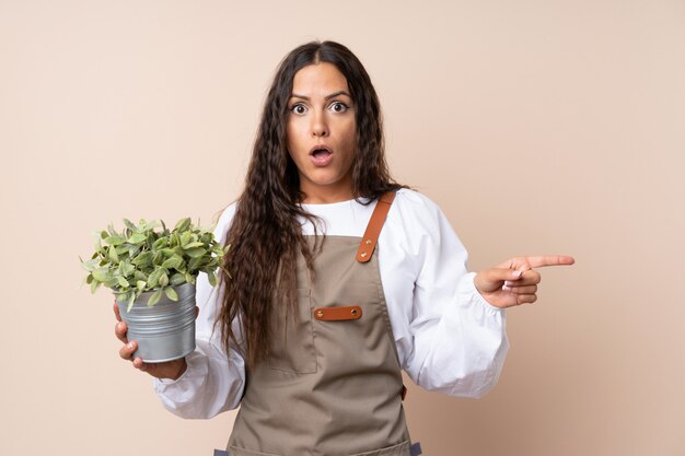 Jovem mulher segurando uma planta surpreso e apontando o lado