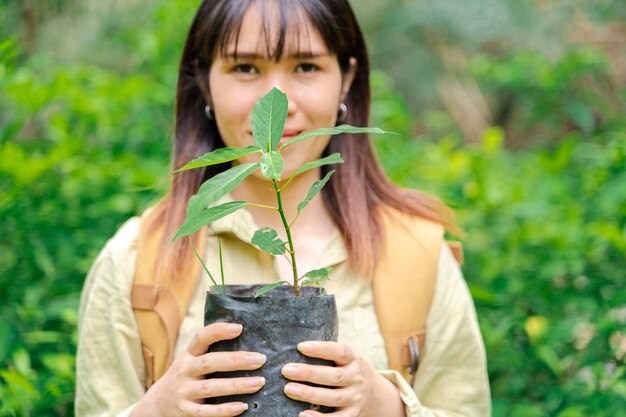 Jovem mulher segurando uma planta verde crescendo no solo agricultora orgânica anônima protegendo uma muda em seu jardim