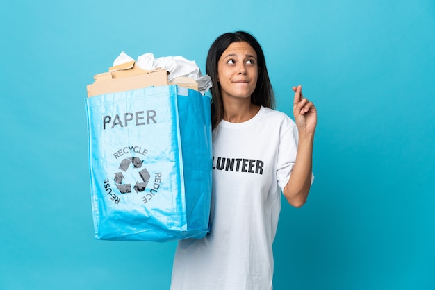 Jovem mulher segurando uma sacola de reciclagem cheia de papel com os dedos se cruzando e desejando o melhor