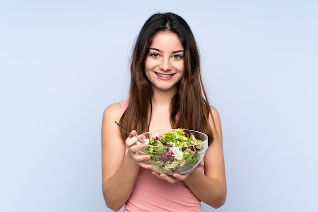Jovem mulher segurando uma salada isolada na parede azul