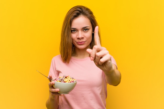 Foto jovem mulher segurando uma tigela de cereais, mostrando o número um com o dedo