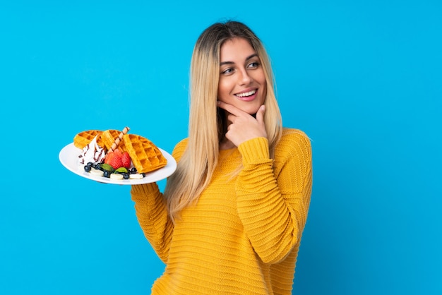 Jovem mulher segurando waffles pensando uma idéia e olhando de lado