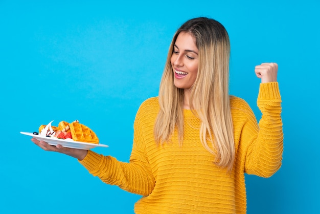 Foto jovem mulher segurando waffles sobre parede isolada comemorando uma vitória