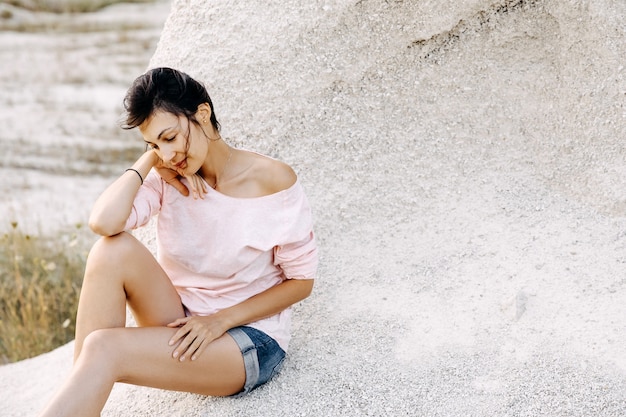 Jovem mulher sentada à beira de um penhasco em uma praia, clima calmo.