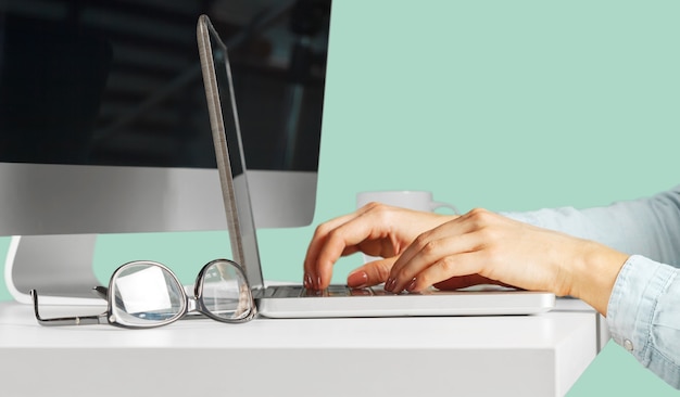 Jovem mulher sentada à mesa com o computador netbook aberto. Pessoa do sexo feminino usando tecnologia moderna.