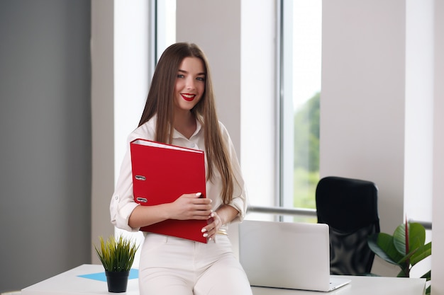 Jovem mulher sentada à mesa com um laptop em um escritório branco. estudante ou empresária