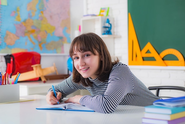 Jovem mulher sentada à mesa fazendo tarefas na biblioteca Retrato de estudante universitário na faculdade Aluna tomando notas de um livro na faculdade