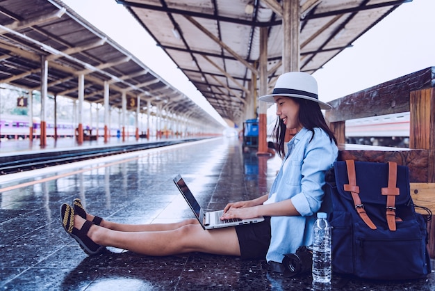 Jovem mulher sentada ao laptop enquanto aguarda o trem