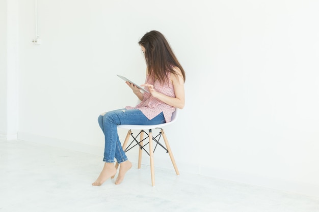 Foto jovem mulher sentada em uma cadeira com tablet digital na parede branca