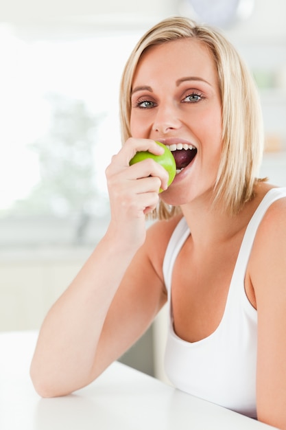 Jovem, mulher, sentada, mesa, comer, verde, maçã, enquanto, olhar, câmera