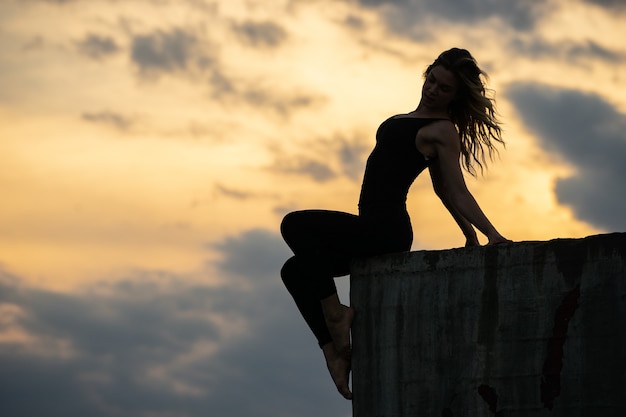 Foto jovem mulher sentada na borda com o nascer do sol.