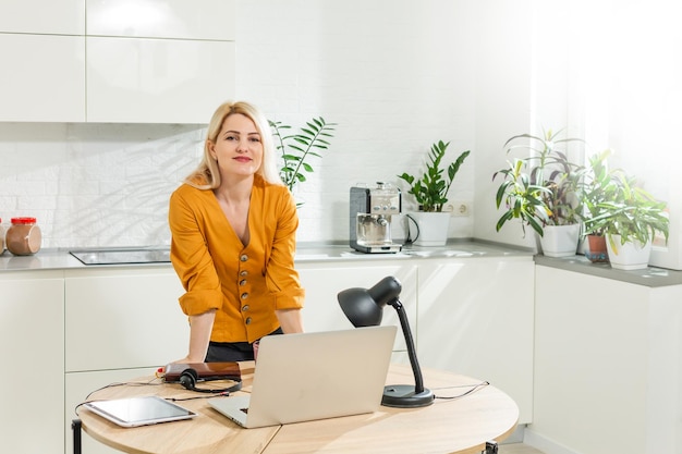 Jovem mulher sentada na cozinha e trabalhando no laptop.