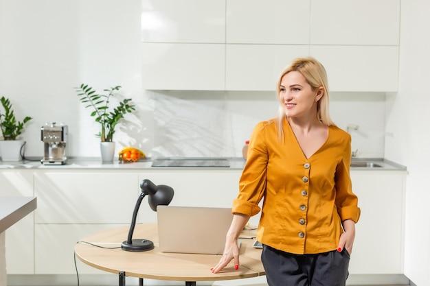 Jovem mulher sentada na cozinha e trabalhando no laptop.