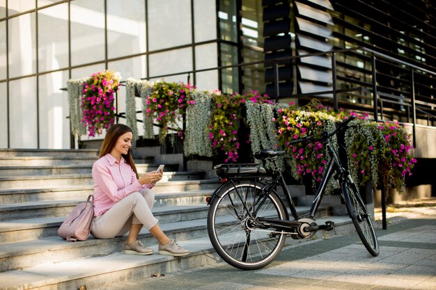 Jovem mulher sentada na escada perto de ebike e usling smartphone