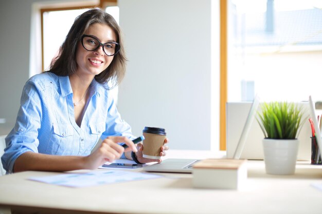 Jovem mulher sentada na mesa do escritório olhando para a tela do computador portátil Jovem mulher