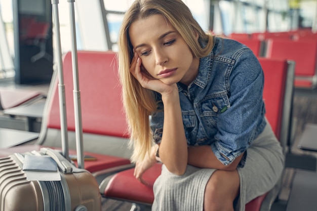 Jovem mulher sentada na zona lounge do aeroporto, com o cotovelo apoiado no joelho