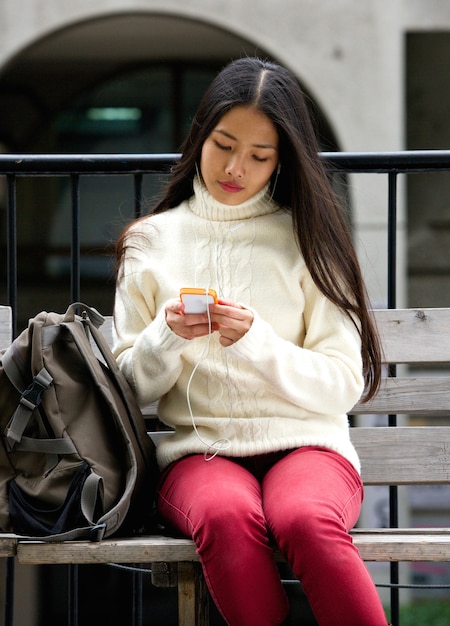 Foto jovem mulher sentada no banco do parque com telefone celular e fones de ouvido