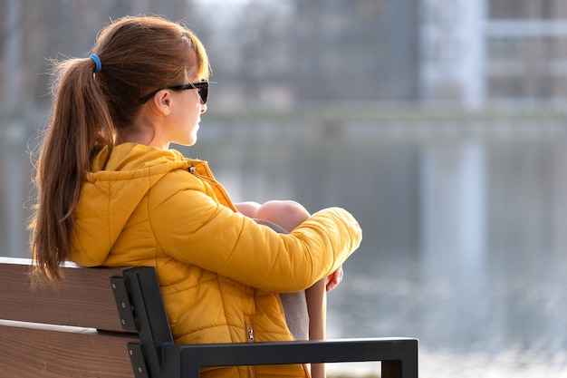 Jovem mulher sentada no banco do parque relaxante num dia quente de primavera.