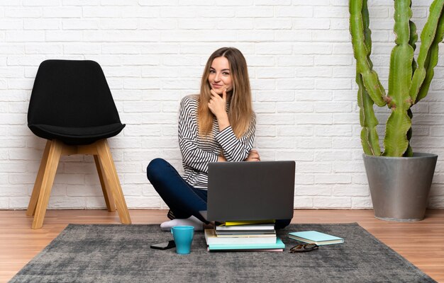 Jovem mulher sentada no chão com o laptop rindo