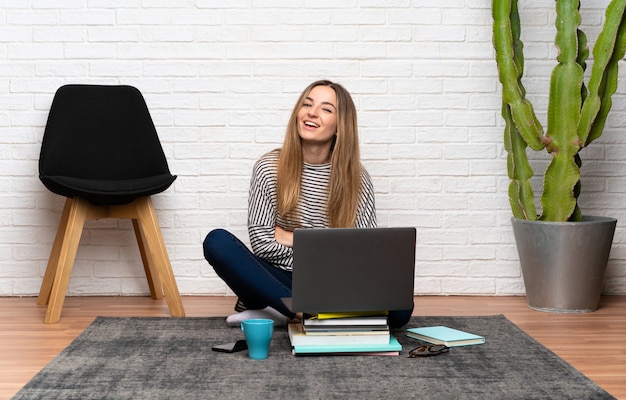 Jovem mulher sentada no chão com o laptop rindo