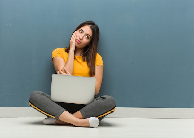 Jovem mulher sentada no chão com um laptop cansado e com muito sono