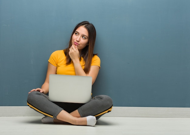 Jovem mulher sentada no chão com um laptop duvidoso e confuso