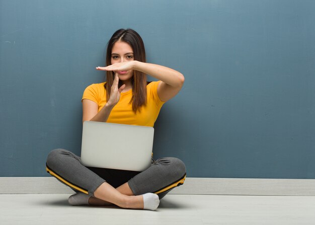 Jovem mulher sentada no chão com um laptop fazendo um gesto de timeout