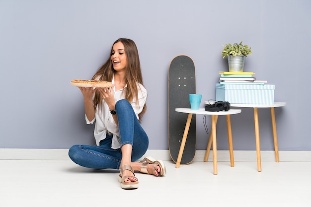 Jovem mulher sentada no chão com uma pizza