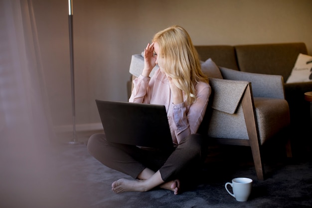 Jovem mulher sentada no chão da sala com o laptop