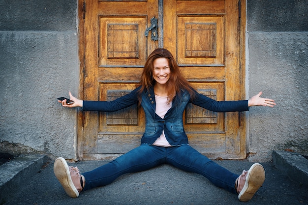 Foto jovem mulher sentada no chão sobre a porta de madeira à moda antiga