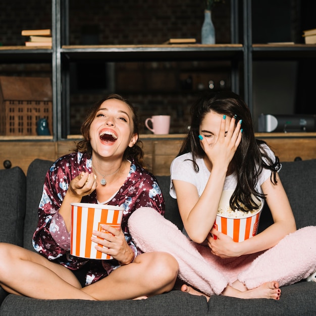 Jovem mulher sentada no sofá rindo enquanto assistia filme