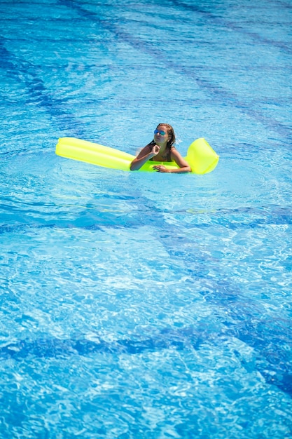 Jovem mulher sexy em um maiô nada na piscina em um colchão inflável. garota de óculos escuros em uma piscina azul de férias