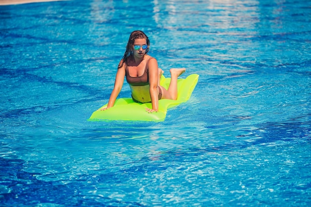 Jovem mulher sexy em um maiô nada na piscina em um colchão inflável Garota em óculos de sol em uma piscina azul de férias