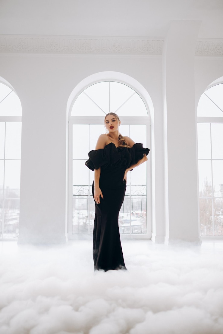 Foto jovem mulher sexy em um vestido longo preto elegante em uma sala iluminada perto da janela