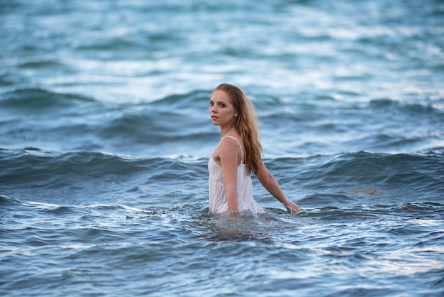 Jovem mulher sexy está nadando no mar azul transparente. Mulher sensual e magro flutuando na água do oceano. Vestido sexy molhado.