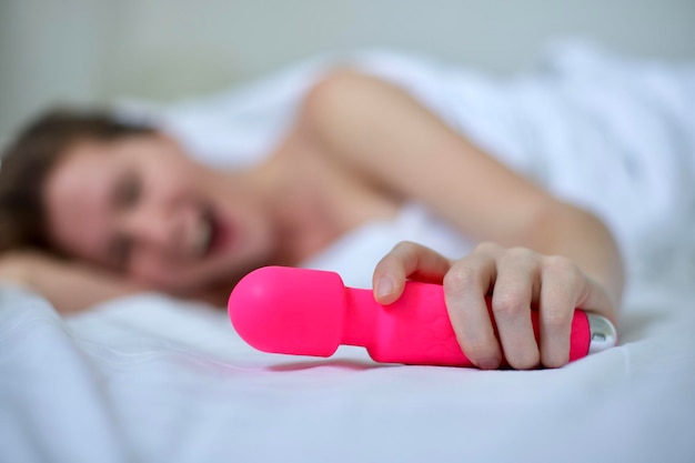 Jovem mulher sexy feliz segura na mão o brinquedo sexual masturba-se com vibrador na cama no quarto em casa