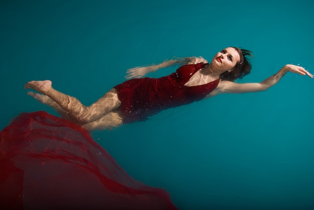 Jovem mulher sexy flutuando na piscina com vestido vermelho. tiro de beleza