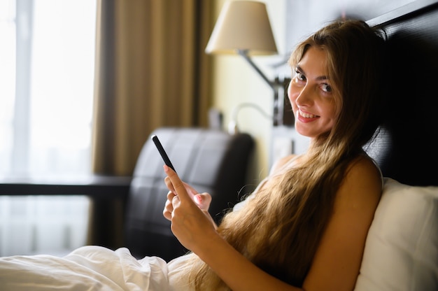 Jovem mulher sexy relaxando com seu smartphone na cama