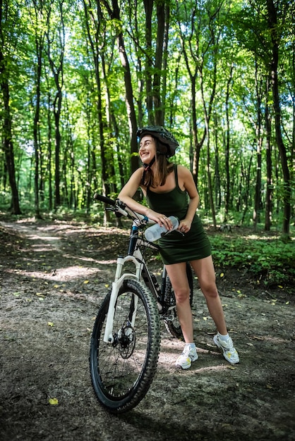 Jovem mulher sexy usa vestido curto verde anda de bicicleta na floresta passa tempo no dia de verão