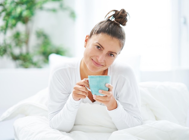 Jovem mulher simpática na cama com caneca de café ou chá