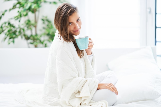 Jovem mulher simpática na cama com caneca de café ou chá