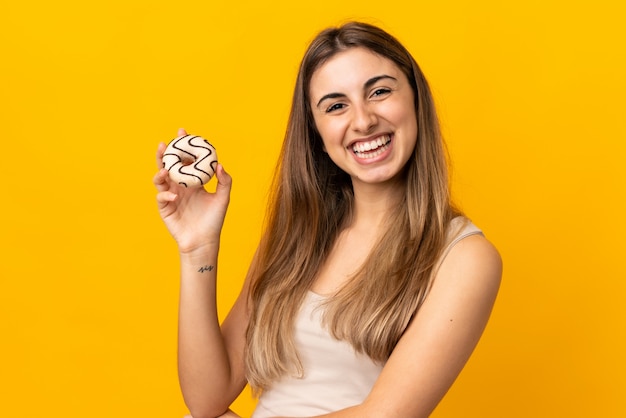 Jovem mulher sobre amarelo isolado segurando uma rosquinha e feliz