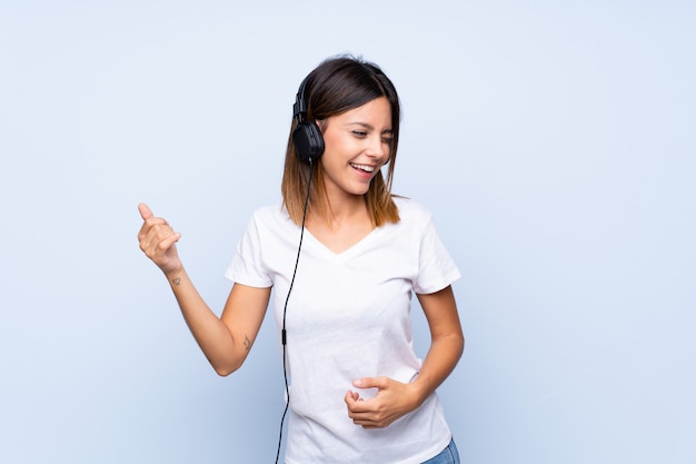 Jovem mulher sobre azul isolado usando o celular com fones de ouvido e dança