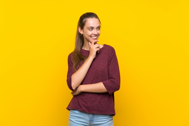 Jovem mulher sobre fundo amarelo isolado, olhando para o lado