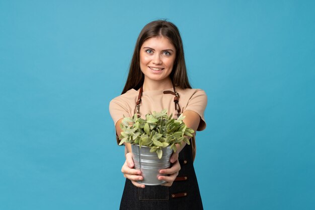 Jovem mulher sobre fundo azul isolado, tomando um vaso de flores